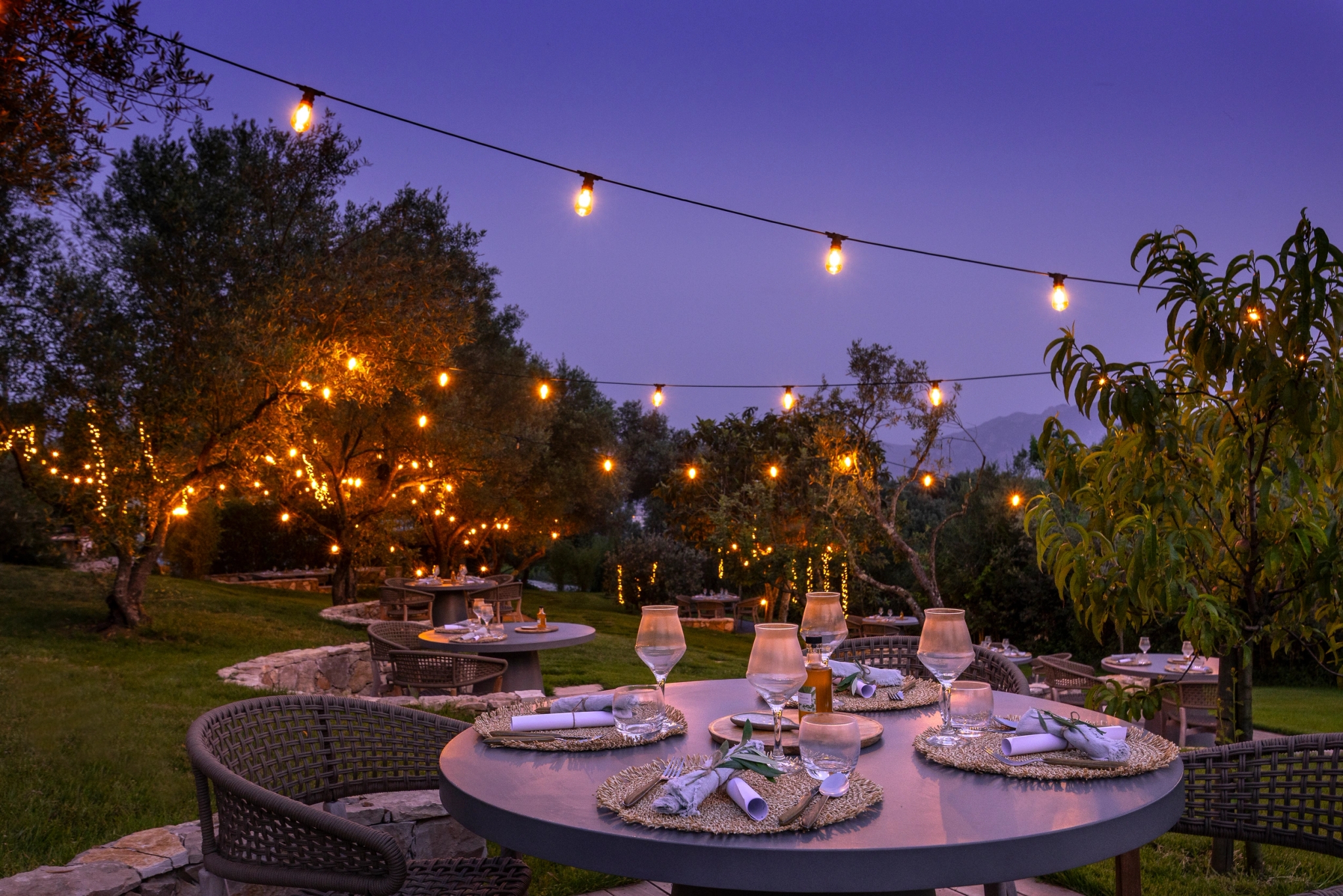 Table de dîner ronde en plein air au crépuscule avec guirlandes lumineuses et décoration élégante dans un jardin
