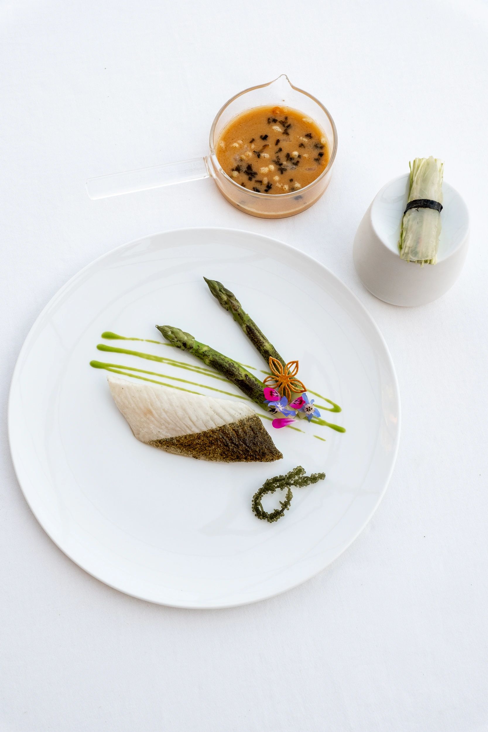 Filet de poisson blanc avec asperges vertes et sauce à la moutarde, présenté sur assiette blanche de restaurant gastronomique