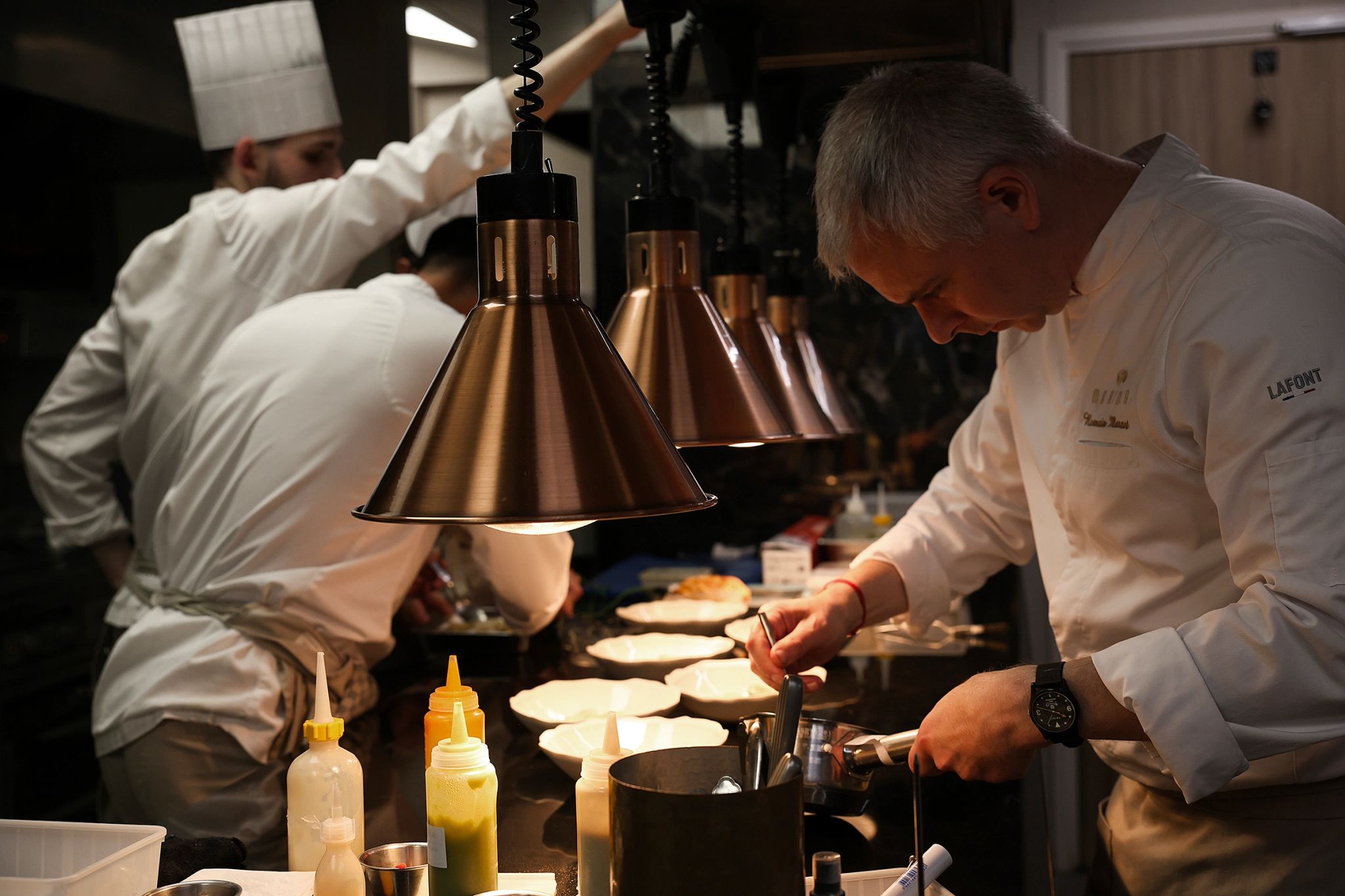 Chef cuisinier préparant un plat en cuisine professionnelle avec lampes chauffantes