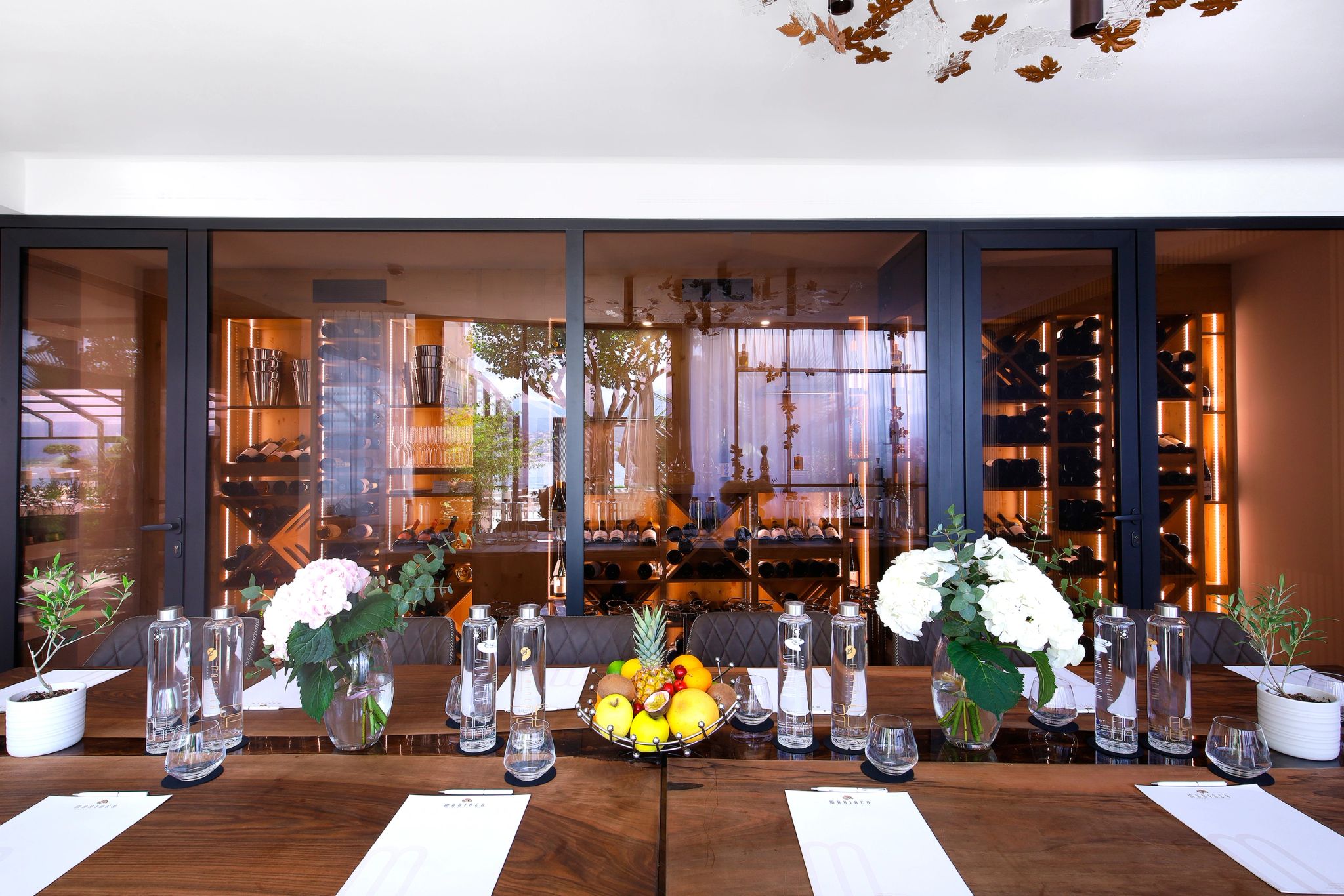 Salle de réunion moderne avec table en bois, fleurs blanches et fruits frais devant de grandes baies vitrées