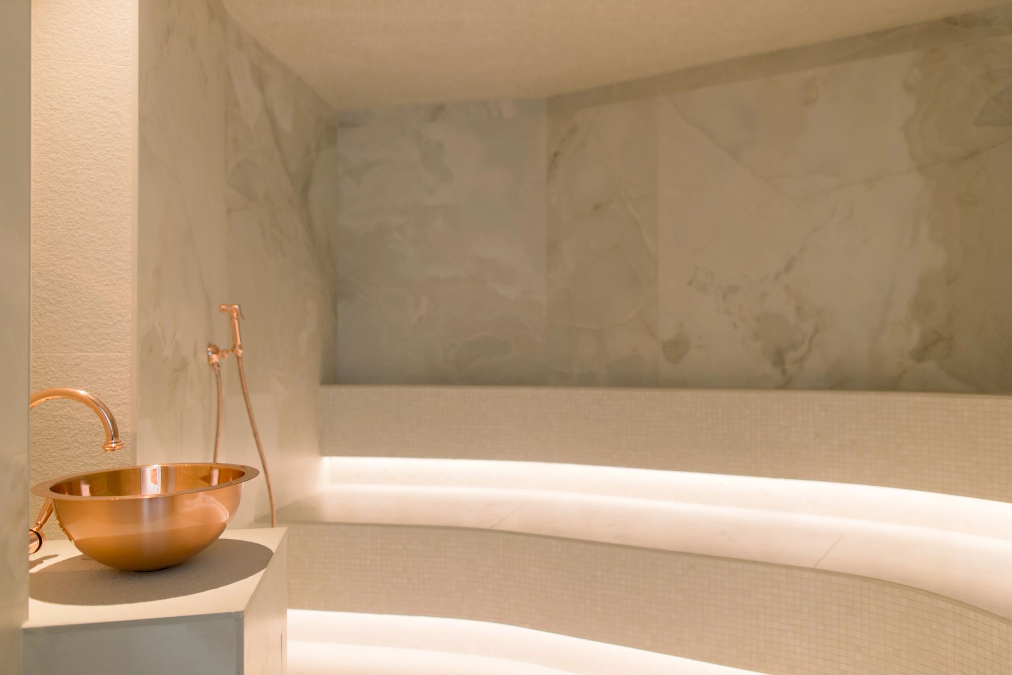 Salle de bain luxueuse avec baignoire moderne, vasque en cuivre et carrelage marbre blanc