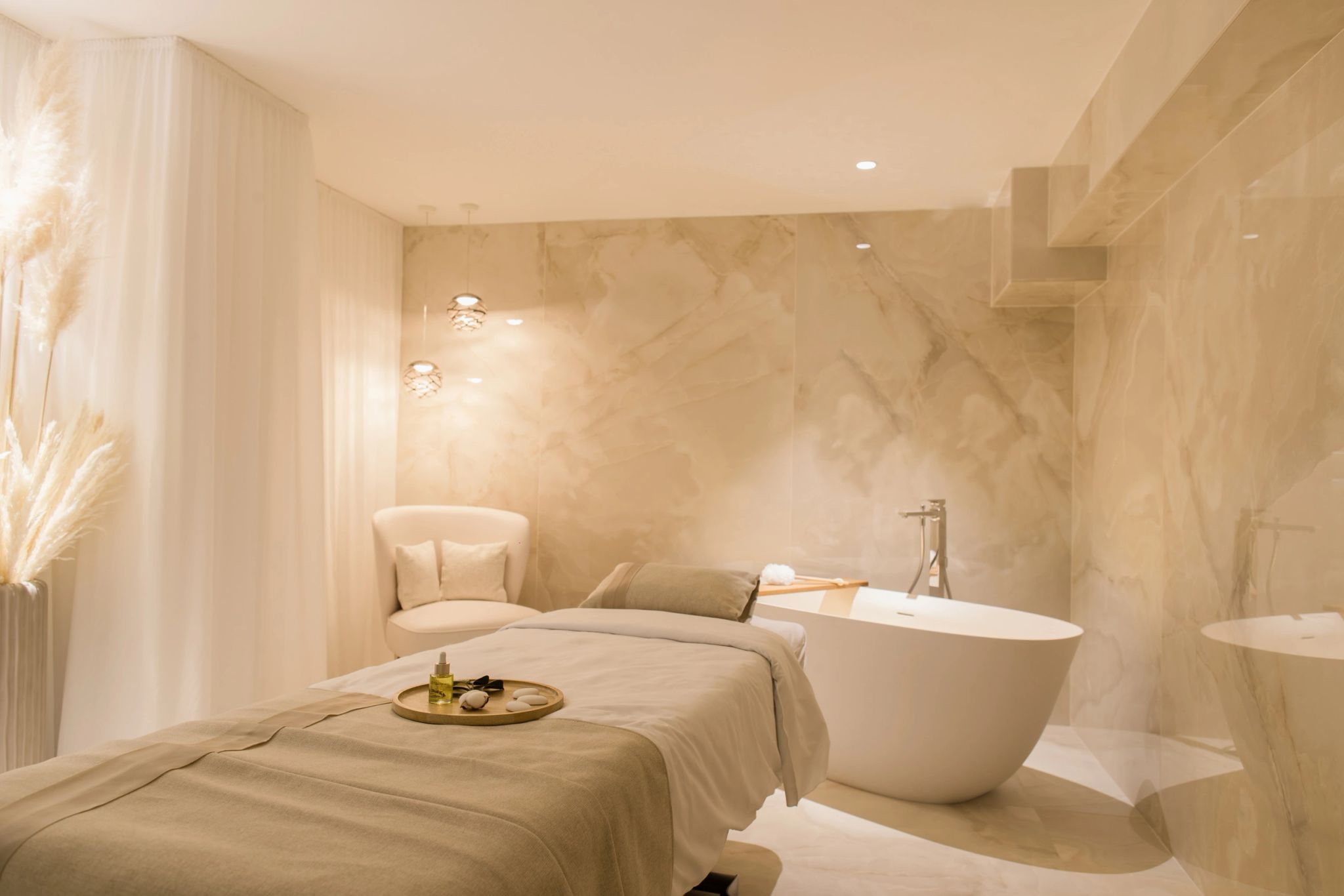 Spa luxueux avec lit de massage, baignoire blanche et marbre beige clair