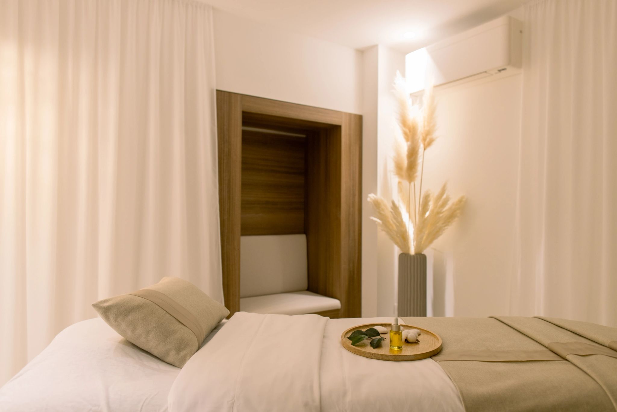Chambre d'hôtel moderne avec lit blanc, décoration minimaliste et vase de fleurs séchées dorées sur table de nuit