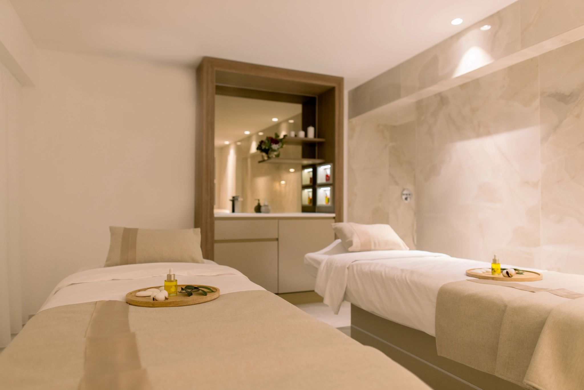 Spa luxueux avec deux lits de massage blanc crème, miroir éclairé et accessoires de détente dorés