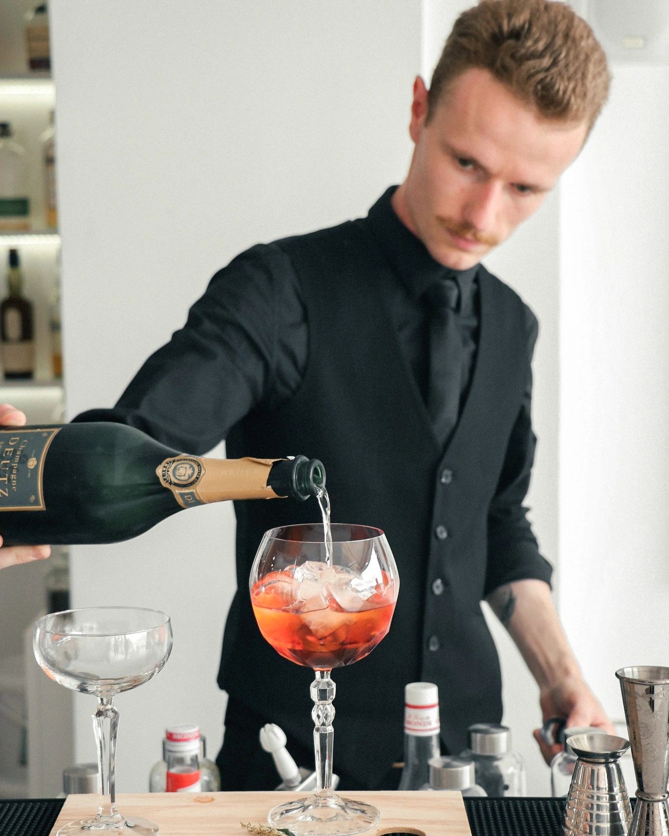 Bartender versant du champagne dans un verre de cocktail rouge avec glaçons