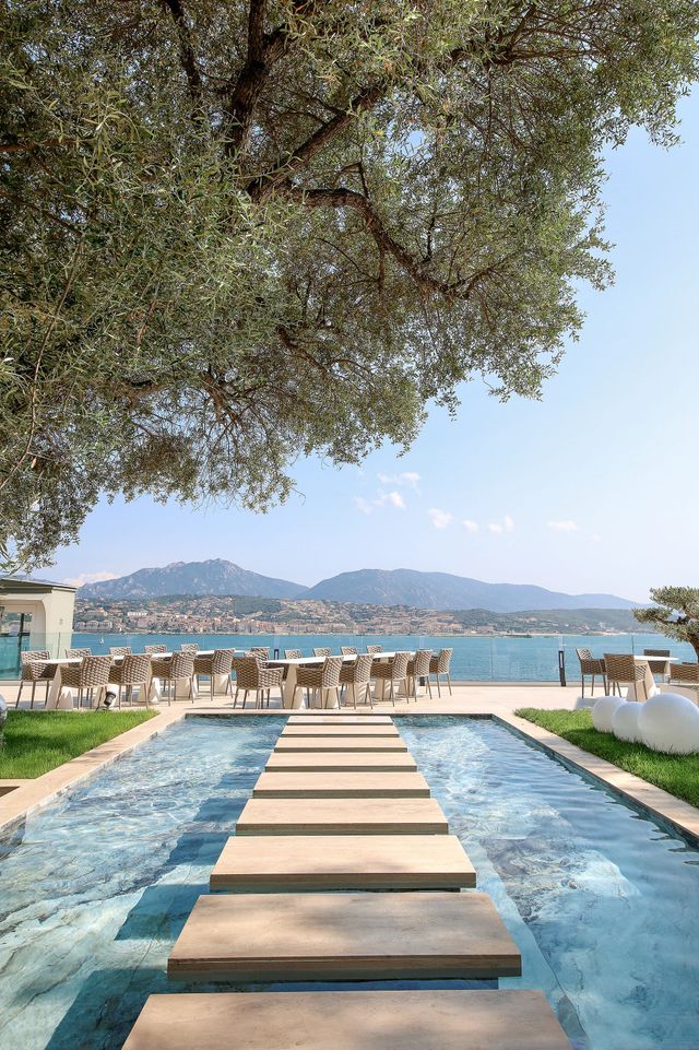 Piscine luxe face à la baie méditerranéenne avec chaises longues et montagnes en arrière-plan