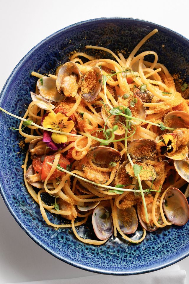Spaghettis aux palourdes avec fleurs comestibles dans un bol bleu
