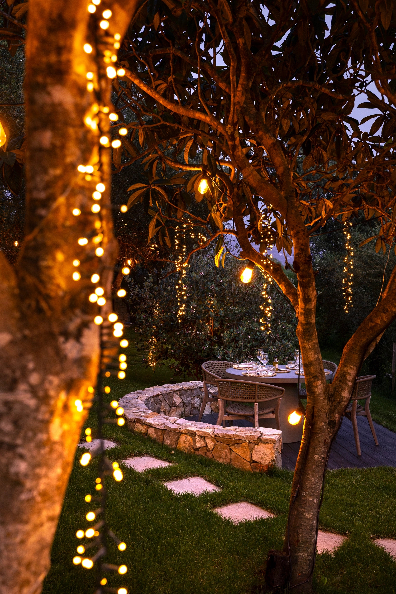 Jardin illuminé la nuit avec guirlandes lumineuses dorées, arbres fruitiers et table de repas sous les étoiles