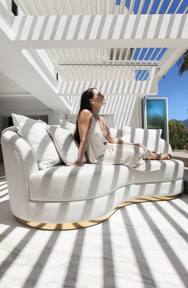 Femme assise sur un canapé blanc dans une terrasse moderne avec pergola et vue sur les montagnes